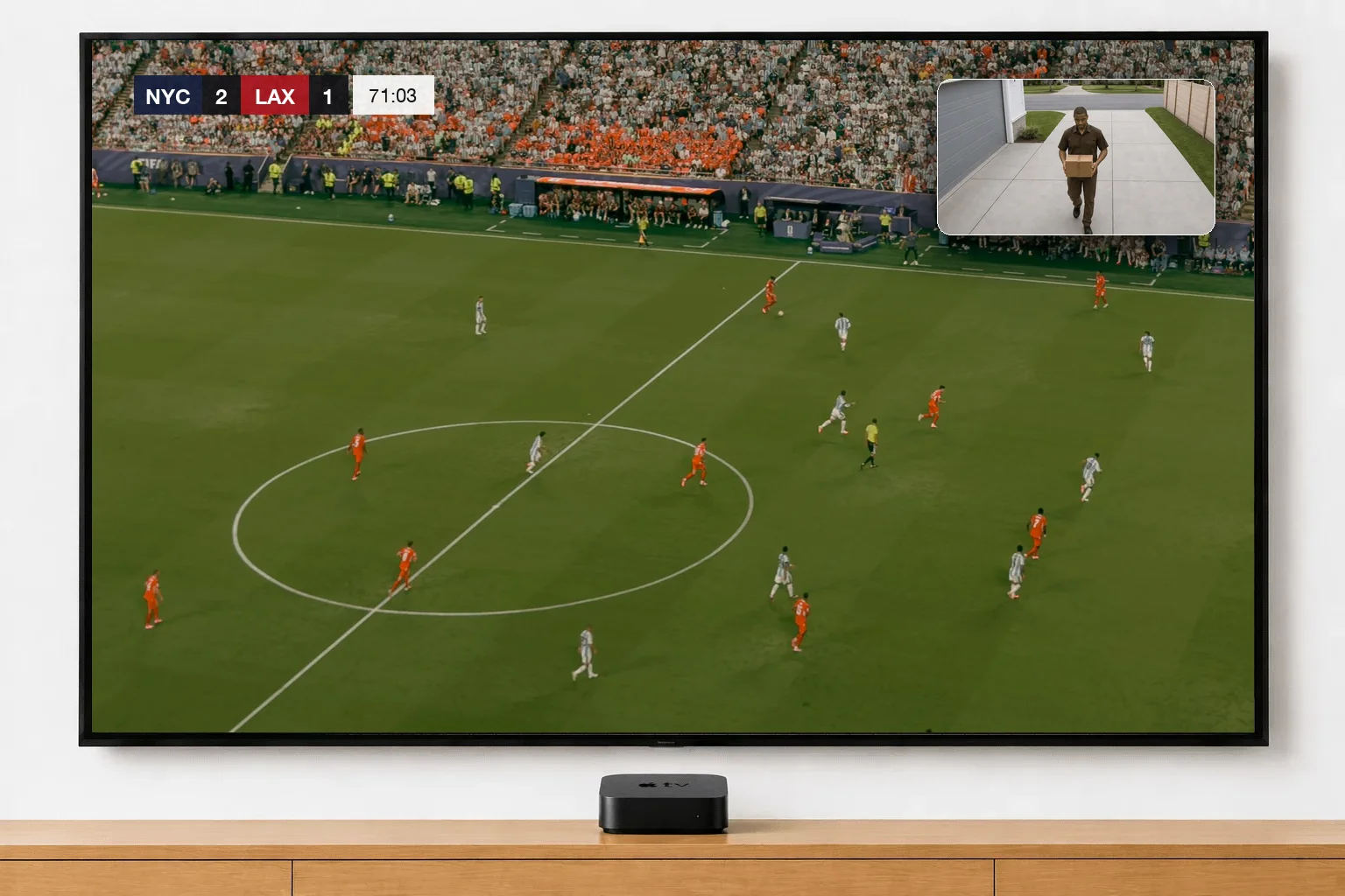 A wall-mounted TV showing a soccer match from the broadcast camera, with the Garage Camera floating in the top-right corner as a delivery driver walks up the driveway